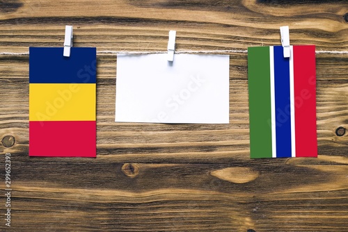 Hanging flags of Chad and Gambia attached to rope with clothes pins with copy space on white note paper on wooden background.Diplomatic relations between countries. photo