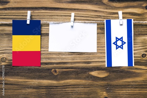 Hanging flags of Chad and Israel attached to rope with clothes pins with copy space on white note paper on wooden background.Diplomatic relations between countries. photo