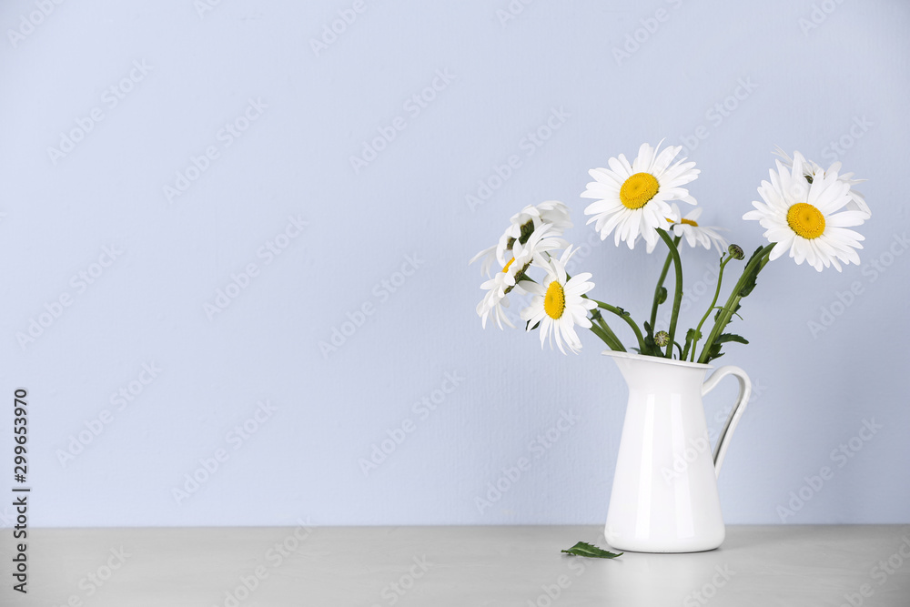 Beautiful tender chamomile flowers in jug on table against light background, space for text