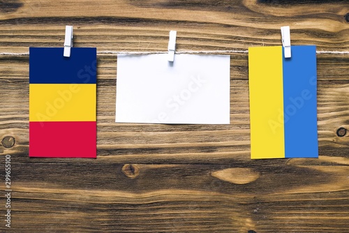 Hanging flags of Chad and Ukraine attached to rope with clothes pins with copy space on white note paper on wooden background.Diplomatic relations between countries. photo