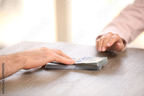 Man giving dollar bills to businesswoman at wooden table, closeup