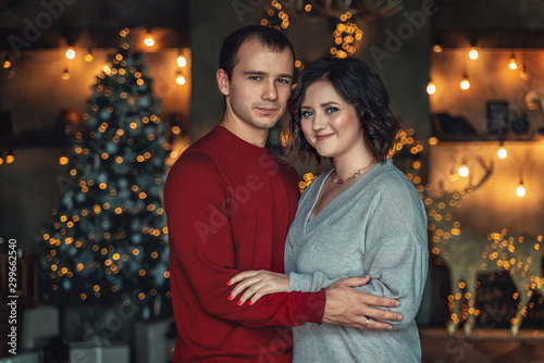 Loving couple stands by the fireplace with a Christmas tree in the New Year