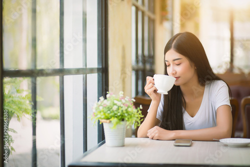 Φωτογραφία A beautiful woman who is sitting drinking coffee near the window with warm sunlight passing through in the morning
