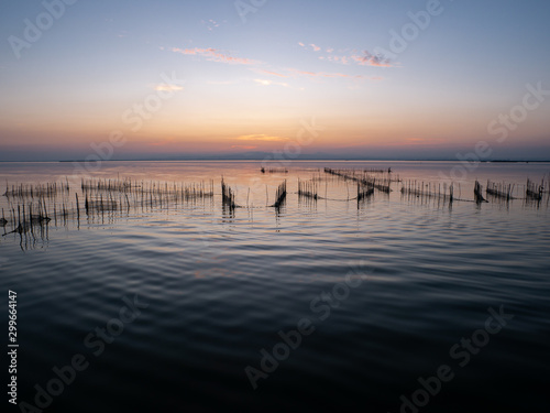  Salty lagoon at sunset with fisherman nets crescent moon and city lights in the background with warm colors and reflections in the water