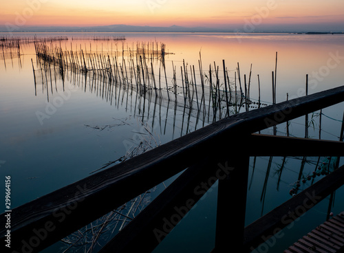 Fototapeta Naklejka Na Ścianę i Meble -   Salty lagoon at sunset with fisherman nets crescent moon and city lights in the background with warm colors and reflections in the water