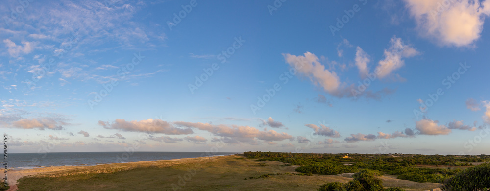 Seaside with sand dunes and colorful sky at sunset.