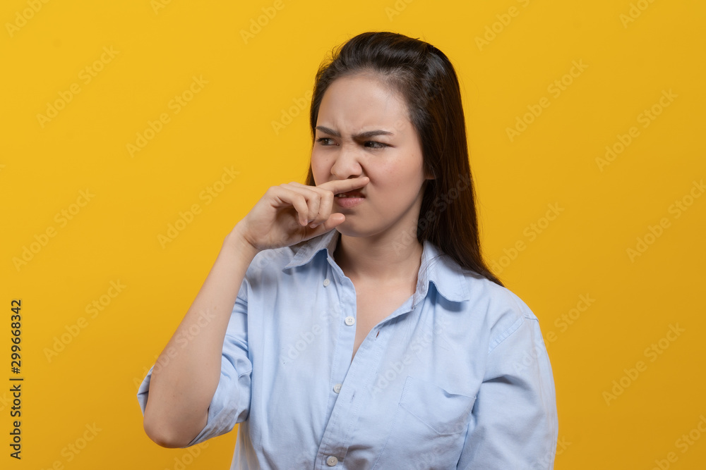 Face expression of human. Asian female smelling disgusted odor and pinching his nose in studio shoot yellow background. Face expression of human. Asian female smelling disgusted odor and pinching his nose in studio shoot yellow background.