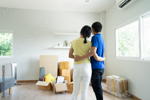 Start your new family in new house. Asian couple hugging together and looking at room in new house with many stuff on the floor after moving in.