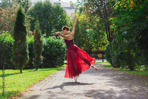 Woman ballerina in red ballet dress dancing in pointe shoes in autumn park. © Smile
