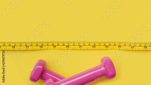 Fitness concept dumbbell and measuring tape on yellow background