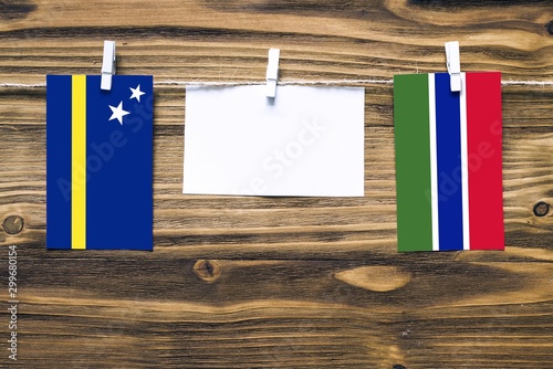 Hanging flags of Curacao and Gambia attached to rope with clothes pins with copy space on white note paper on wooden background.Diplomatic relations between countries. photo