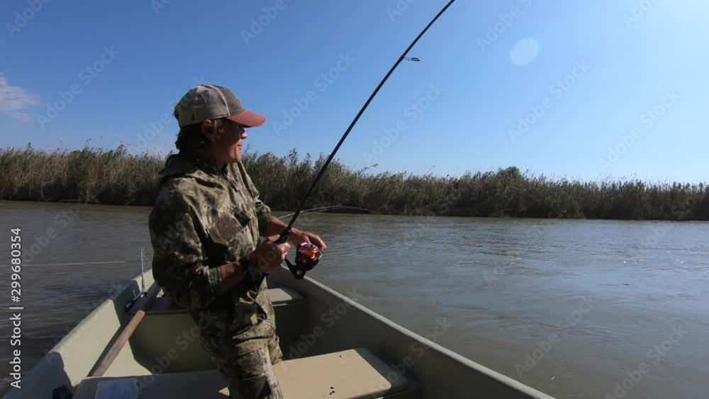 Fisherman catches fish from the boat, angler stands in the boat, spins the reel and holds the bended rod Fisherman catches fish from the boat, angler stands in the boat, spins the reel and holds the bended rod