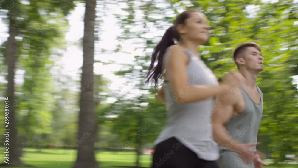Panning shot of young athletic couple in sportswear running in park together while exercising in summer morning Panning shot of young athletic couple in sportswear running in park together while exercising in summer morning