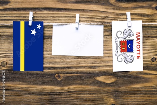 Hanging flags of Curacao and Mayotte attached to rope with clothes pins with copy space on white note paper on wooden background.Diplomatic relations between countries. photo