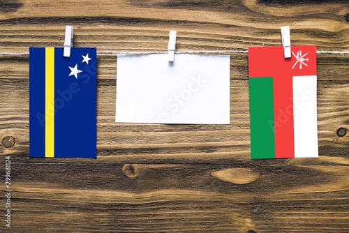 Hanging flags of Curacao and Oman attached to rope with clothes pins with copy space on white note paper on wooden background.Diplomatic relations between countries. photo