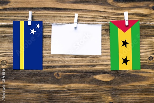 Hanging flags of Curacao and Sao Tome And Principe attached to rope with clothes pins with copy space on white note paper on wooden background.Diplomatic relations between countries. photo