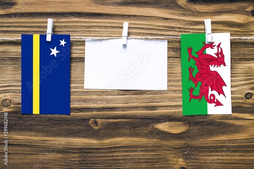 Hanging flags of Curacao and Wales attached to rope with clothes pins with copy space on white note paper on wooden background.Diplomatic relations between countries. photo