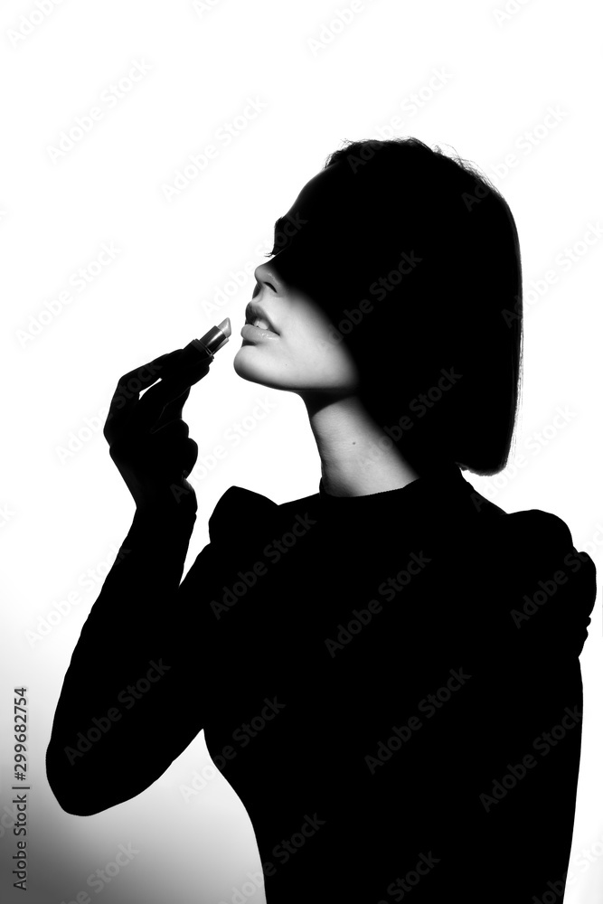 Fashion advertising portrait of a young beautiful girl using lipstick. Black and white silhouette with epic light. Fashion advertising portrait of a young beautiful girl using lipstick. Black and white silhouette with epic light.
