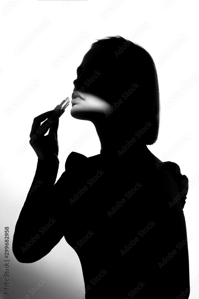 Fashion advertising portrait of a young beautiful girl using lipstick. Black and white silhouette with epic light. Fashion advertising portrait of a young beautiful girl using lipstick. Black and white silhouette with epic light.