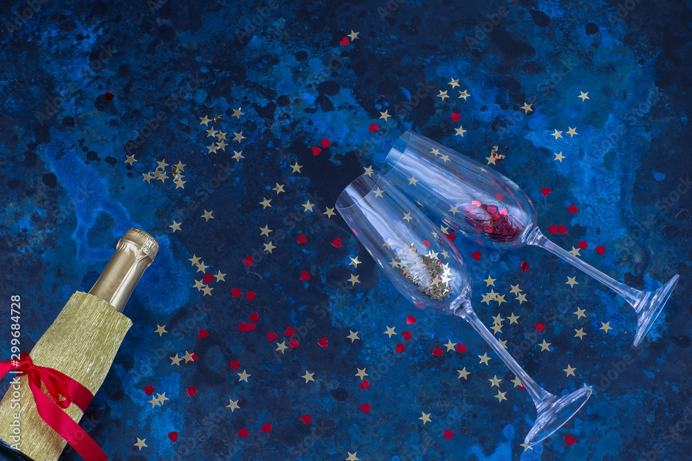 Fototapeta premium champagne bottle, two glasses and confetti on a dark blue background