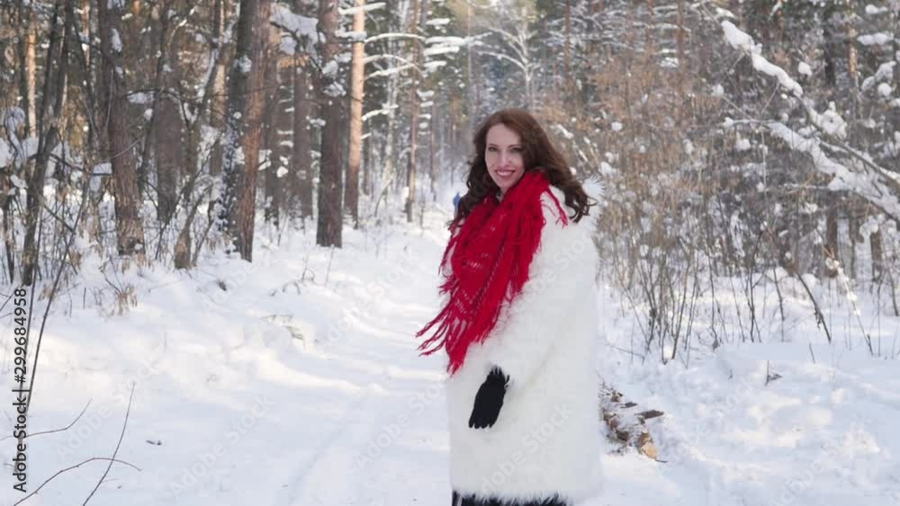 Attractive blonde in a white fur coat and red scarf posing on the background of a winter forest. Model in a white fur coat on a snowy background Attractive blonde in a white fur coat and red scarf posing on the background of a winter forest. Model in a white fur coat on a snowy background