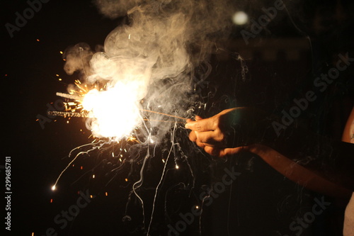 human Hand holding the sparkler on sparkling with dark background with some white smoke on the deepavali / dewali celebration