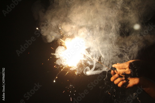 human Hand holding the sparkler on sparkling with dark background with some white smoke on the deepavali / dewali celebration