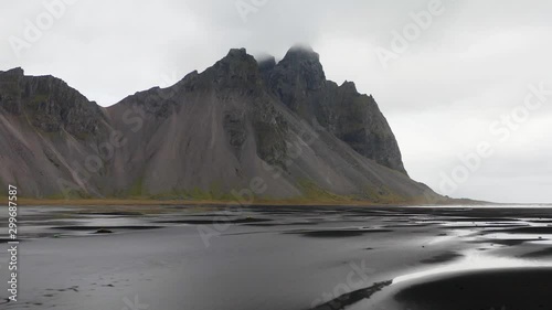 Drone video flying towards Vestrahorn mountain in south-east Iceland. The mountain is reflecting in pools of water on the sand. photo