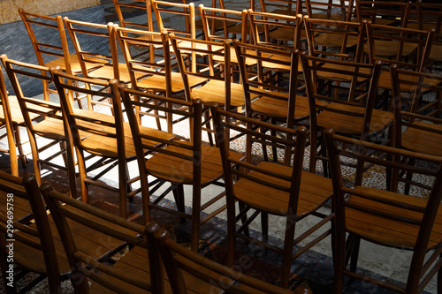 Rows of empty wooden chairs, partly illuminated by sun and partly in shadow, on the terrazzo floor of a church. Light and dark.