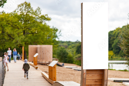 Blank vertical information sign on wooden stand in park in front wooden footpath photo