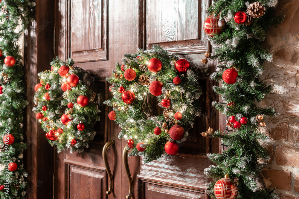 House entrance decorated for holidays. Christmas decoration. Two wreaths and garland of fir tree branches. Large wooden door