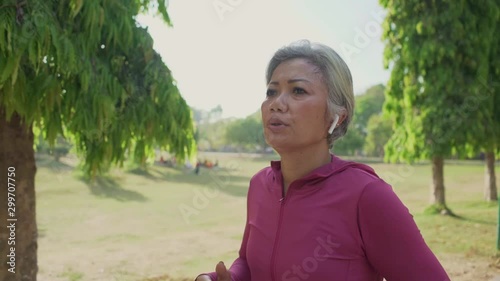 slow motion gimbal tracking shot on attractive middle aged lady running happy at city park . beautiful and sporty 40s woman exercising doing jogging workout enjoying healthy lifestyle and fitness