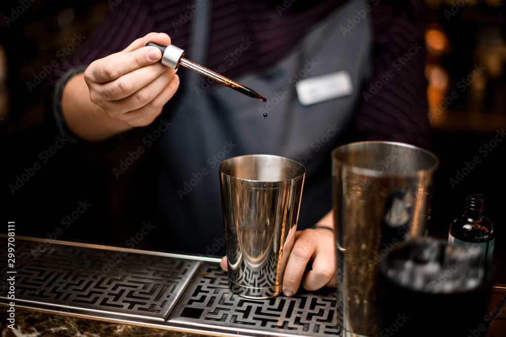 Professional bartender adding a brown essence to an alcoholic drink in a steel shaker