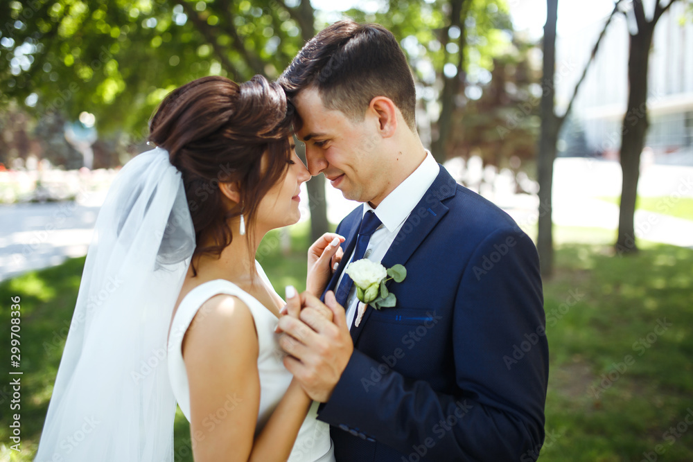 The bride and groom walk together in the park. Charming bride in a white dress, the groom is dressed in a dark elegant suit. Pretty bride and stylish groom. Wedding day. Marriage. The bride and groom walk together in the park. Charming bride in a white dress, the groom is dressed in a dark elegant suit. Pretty bride and stylish groom. Wedding day. Marriage.