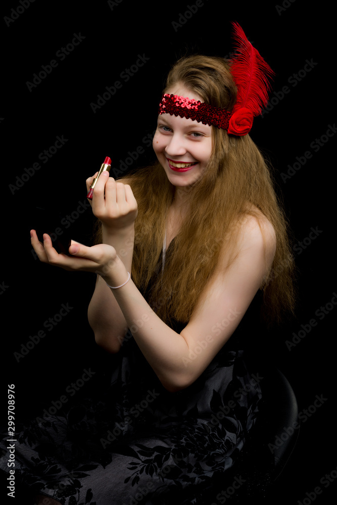 Naklejka premium Beautiful girl of school age paints lips with lipstick and looks