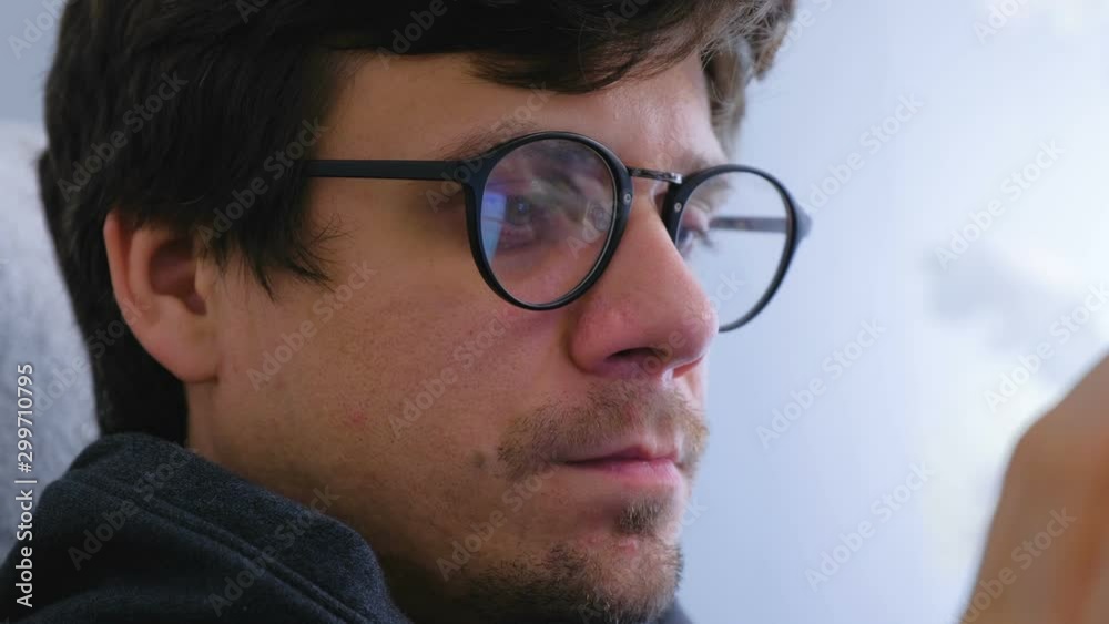 Man in glasses is browsing in social media on smartphone sitting in armchair. Face close-up Man in glasses is browsing in social media on smartphone sitting in armchair. Face close-up