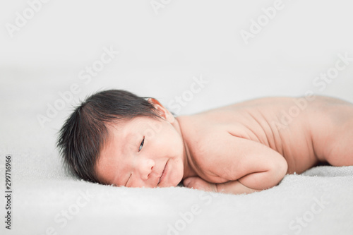 Happy cute adorable Asian baby boy with black hair lying on a white bed.