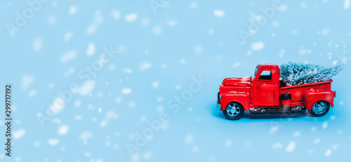 Red truck car carrying a Christmas fir tree with garland on the snow blue background. Concept for magic fairytale Merry Christmas and Winter holidays. Copy space Place text. Snow bokeh