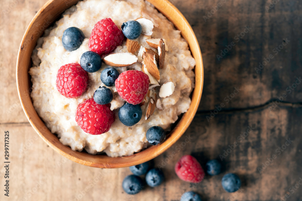 Wheat porridge with almonds, blue and red berries on top. Wooden bowl and wooden rustic backdrop. Food photography, healthy living and lifestyle concept. Wheat porridge with almonds, blue and red berries on top. Wooden bowl and wooden rustic backdrop. Food photography, healthy living and lifestyle concept.