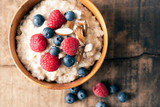 Wheat porridge with almonds, blue and red berries on top. Wooden bowl and wooden rustic backdrop. Food photography, healthy living and lifestyle concept.