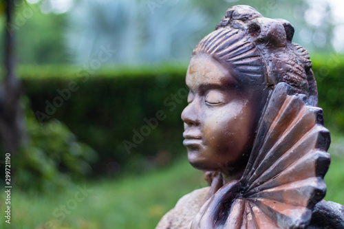 high angle side view of a traditional japanese woman statue in meditation with hand fan and green background. Peace and meditation concept