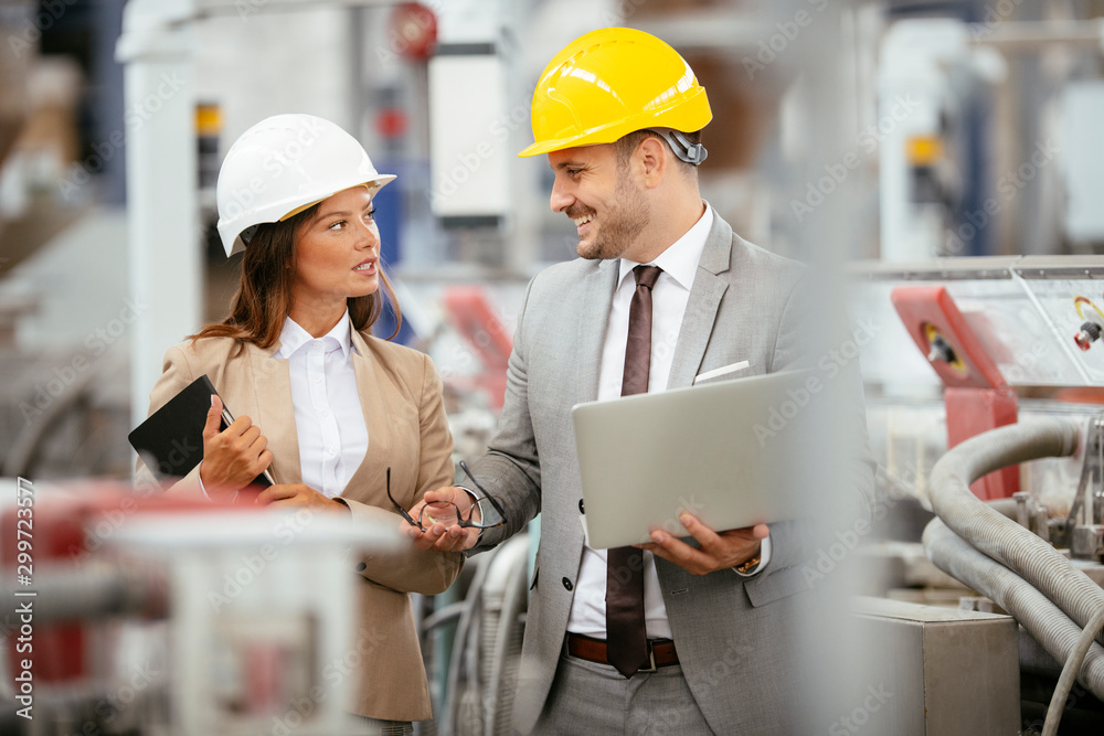 Businessman and businesswoman in factory. Man and woman in suits with helmets in factory discussing work. Businessman and businesswoman in factory. Man and woman in suits with helmets in factory discussing work.