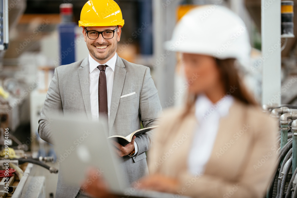 Businessman and businesswoman in factory. Man and woman in suits with helmets in factory discussing work. Businessman and businesswoman in factory. Man and woman in suits with helmets in factory discussing work.