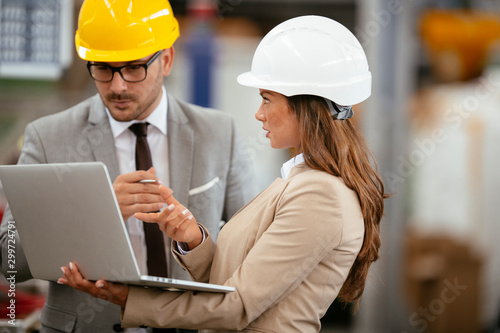 Businessman and businesswoman in factory. Man and woman in suits with helmets in factory discussing work.
