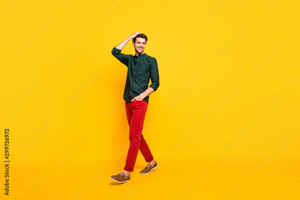 Full length body size turned photo of cheerful youngster stepping away from where he is looking wearing shoes adjusting his hair isolated over vivid color background