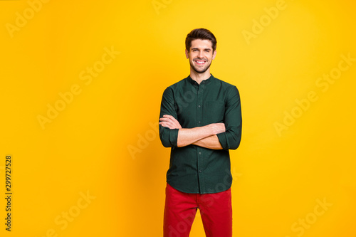 Photo of cheerful positive nice man with good mood standing confidently with arms crossed smiling toothily with bristle growing on face wearing red pants isolated vibrant color background