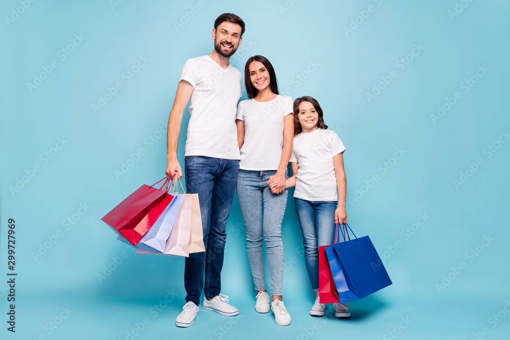 Full length photo of positive three people mommy daddy schoolkid addicted with brown hair shop hold hand hug embrace wear white t-shirt denim jeans sneakers isolated over blue color background