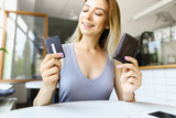 Blonde girl sitting at cafe and keeping wallet with debit card.