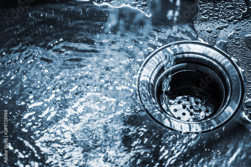 stream of clean water pouring into a steel sink in the kitchen. Toned image photo