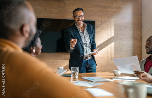 Businessman standing, pointing and smiling to fellow african coworkers in boardroom meeting photo